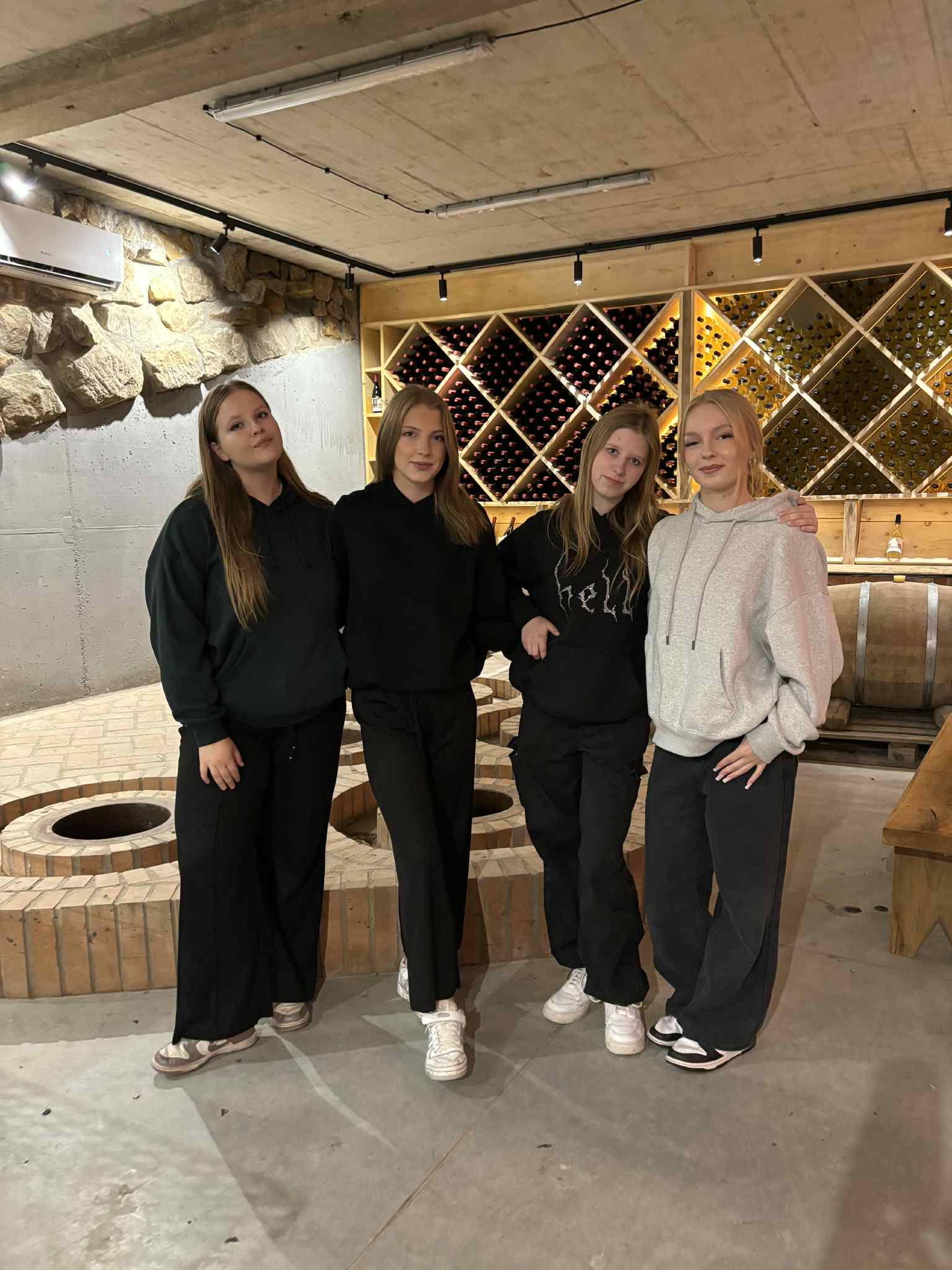 cztery dziewczyny siedzą na szerokich kamiennych schodach w winnicy Talaska. Za dziewczynami widać rzędy winorośli i drewnianą beczkę, a w tle rosną wysokie drzewa.