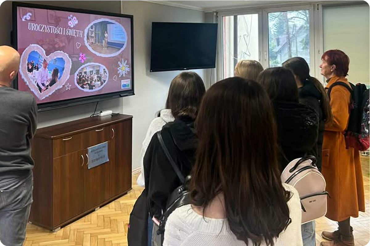 Goście odwiedzający internat oglądają prezentację multimedialną przedstawiającą uroczystości i wydarzenia organizowane dla mieszkańców placówki. Spotkanie odbywa się w jasnej sali wyposażonej w nowoczesny ekran i miejsca do wspólnego spędzania czasu.