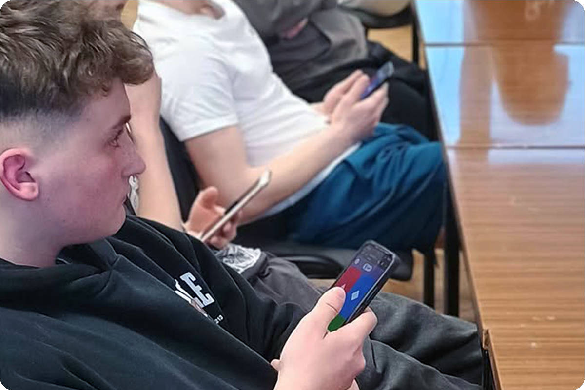 Uczestnicy siedzą przy stole i korzystających ze smartfonów podczas rozgrywki w quizie. Wszyscy skupiają się na ekranach telefonów, prawdopodobnie odpowiadając na pytania w czasie rzeczywistym. Zdjęcie oddaje klimat wspólnej rywalizacji i integracji grupy.