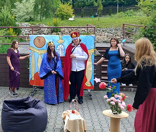 Na zdjęciu widać uczniów odgrywających scenę przedstawienia teatralnego w plenerze. Uczestnicy występują na świeżym powietrzu, wcielając się w swoje role i prezentując spektakl przed publicznością lub w ramach zajęć.